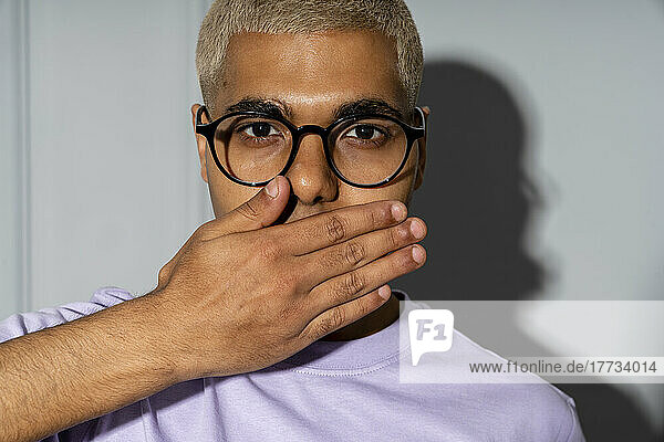 Young man covering mouth with hand in front of wall