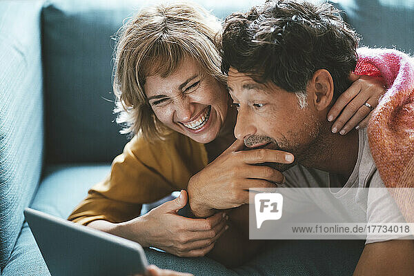Happy mature woman lying with man using digital tablet on sofa at home
