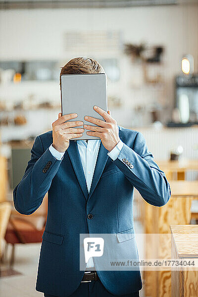 Freelancer covering face with tablet PC at cafe