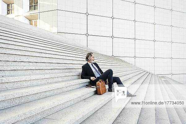 Reifer Geschäftsmann sitzt mit Tasche auf Stufen