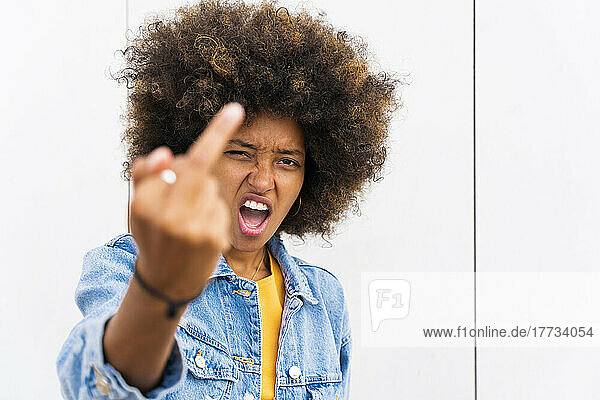 Afro woman showing finger in front of wall