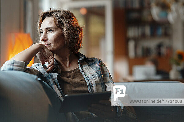 Nachdenkliche Frau mit Tablet-PC sitzt zu Hause auf dem Sofa