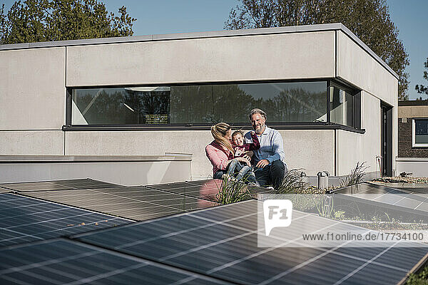 Glückliches Mädchen mit Eltern  die am Solarpanel auf dem Dach sitzen