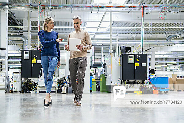 Businessman with digital tablet and businesswoman walking and talking in factory