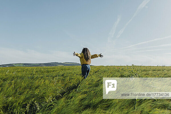 Young woman standing with arms outstretched in meadow