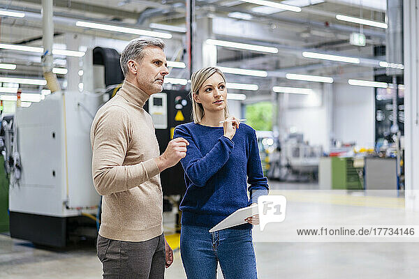 Businessman and businesswoman with digital tablet talking in factory