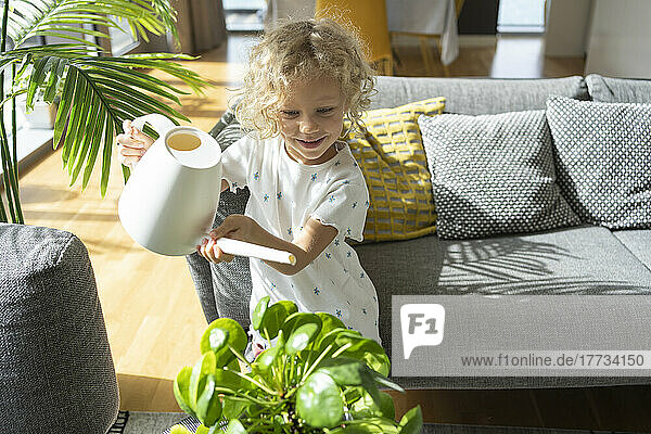 Girl watering plant in living room at home