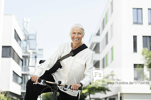 Smiling businesswoman with bicycle in front of buildings