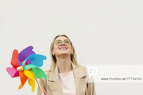 Smiling woman looking up holding colorful pinwheel toy against white background
