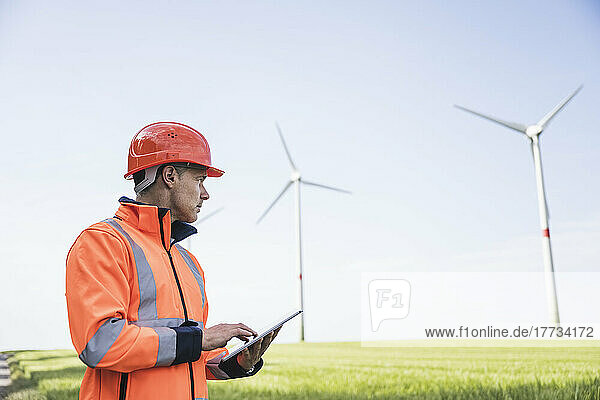 Engineer holding tablet PC at field wind turbine