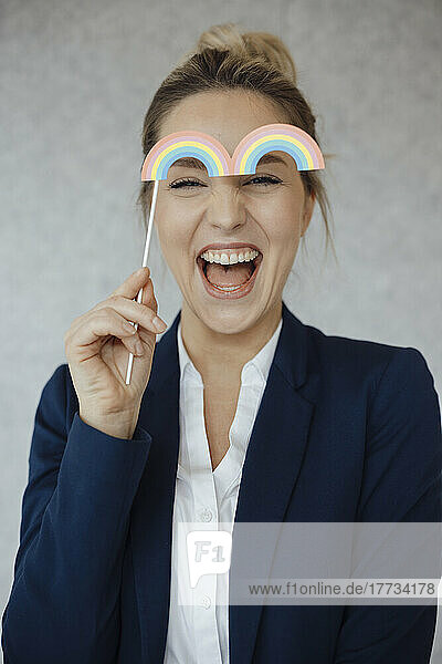 Happy businesswoman holding rainbow prop in office