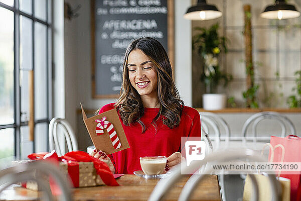 Happy beautiful woman reading Christmas card sitting in cafe