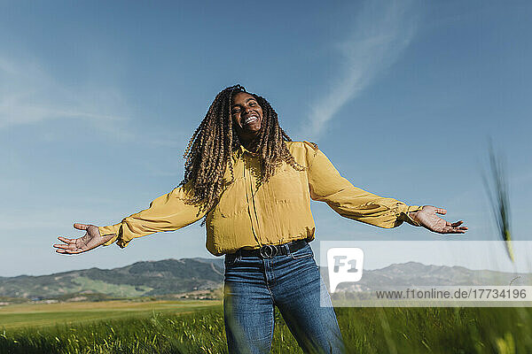 Happy woman standing with arms outstretched in meadow