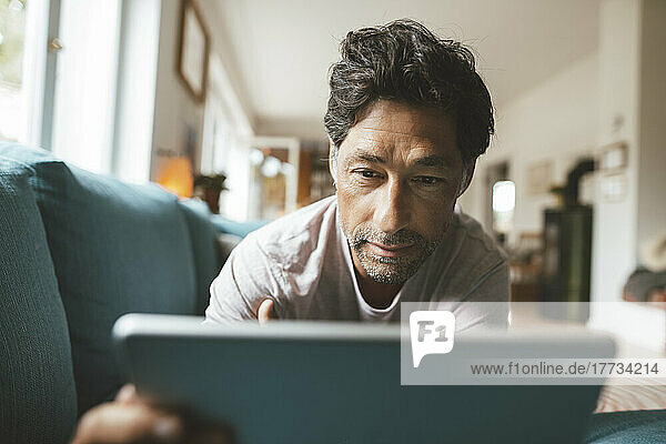 Mature man using tablet PC on sofa at home