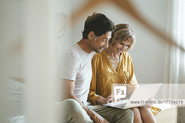 Happy woman using laptop sitting by man at home