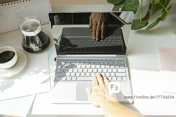 Hands of freelancer typing on laptop at desk in home office
