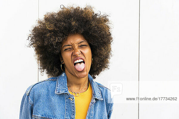 Afro woman sticking out tongue in front of wall