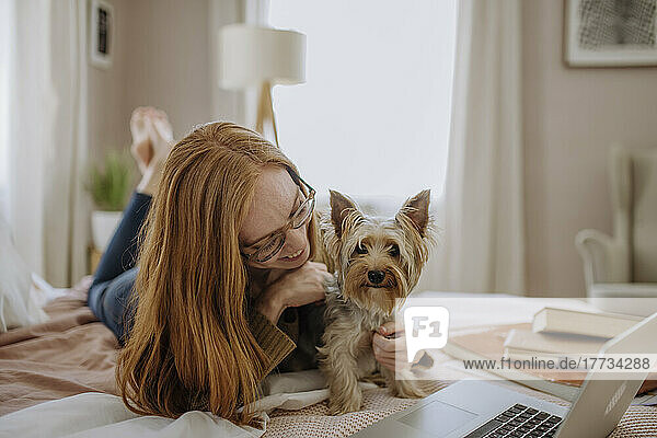 Smiling woman playing with pet dog lying on bed at home