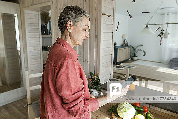 Woman in kitchen at home holding smartphone
