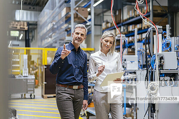 Businessman and businesswoman with digital tablet talking in factory