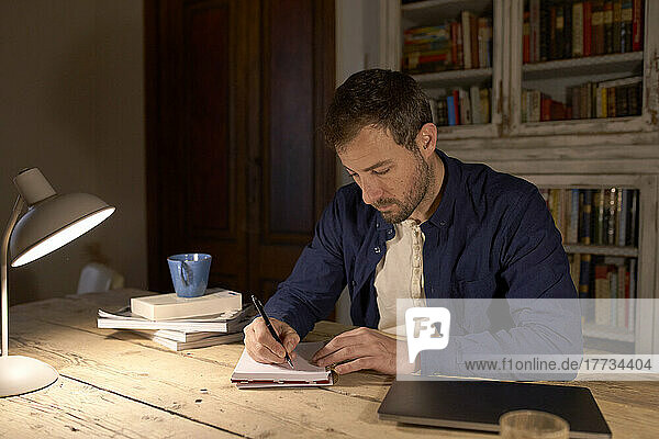Freelancer writing in diary on desk at home