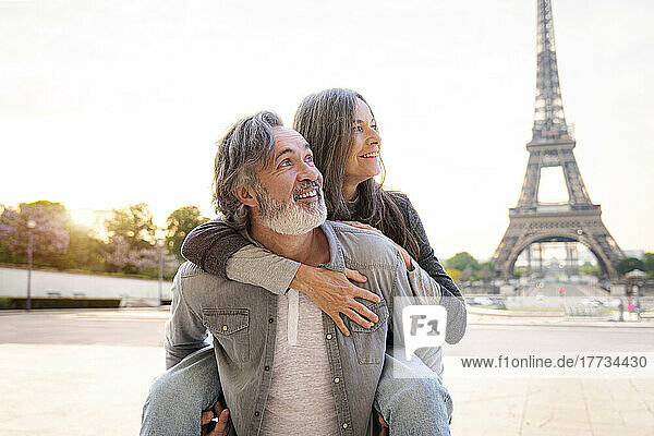 Lächelnder reifer Mann  der einer Frau Huckepackfahrt vor dem Eiffelturm  Paris  Frankreich  gibt