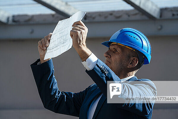 Geschäftsmann mit Schutzhelm analysiert Bauplan auf Baustelle