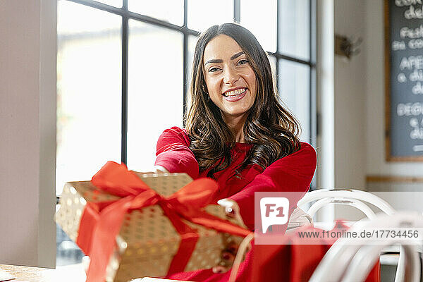 Happy woman giving Christmas present sitting in cafe