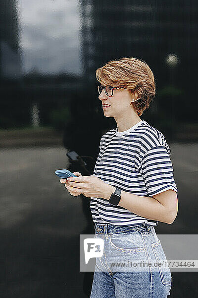 Woman contemplating holding smart phone in front of black wall
