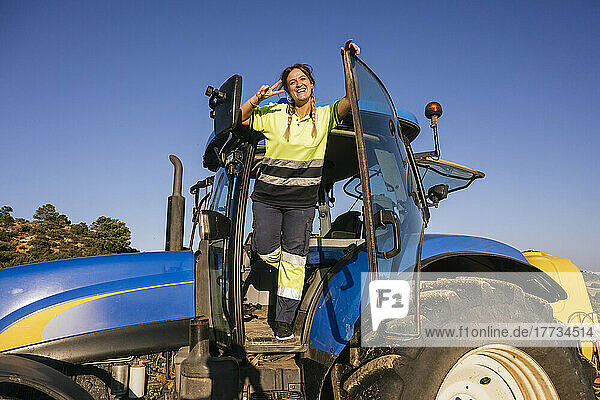 Happy female farmer gesturing peace sign standing in tractor