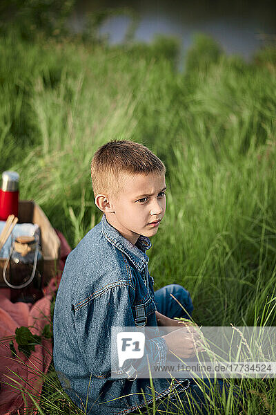 Thoughtful boy sitting on grass in agricultural field