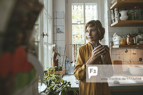 Mature woman with bowl standing in kitchen at home