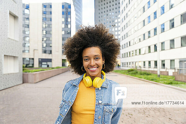 Smiling beautiful Afro woman wearing wireless headphones standing on footpath