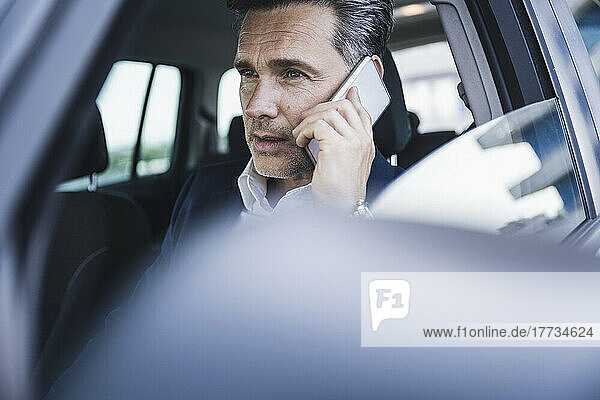 Mature businessman talking on smart phone sitting in car