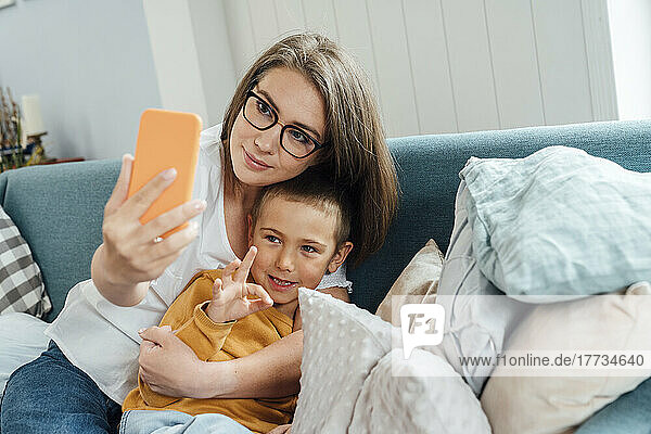 Lächelnde Frau mit Sohn  die zu Hause ein Selfie per Smartphone macht