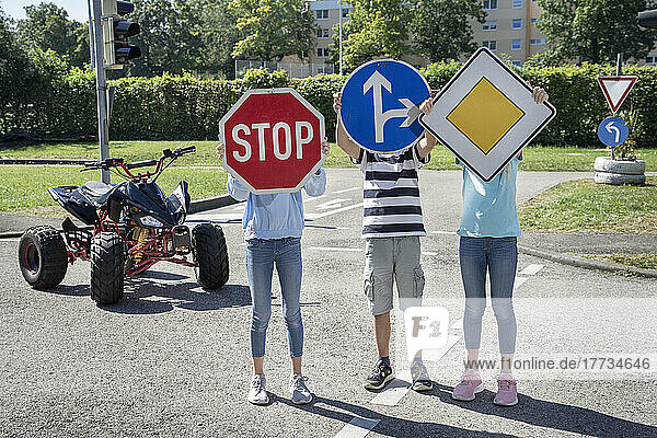 Children holing road signs in front of face standing on road