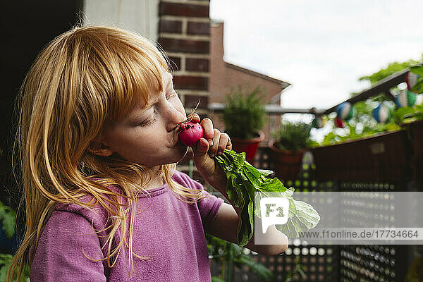 Girl with eyes closed kissing fresh radish on balcony
