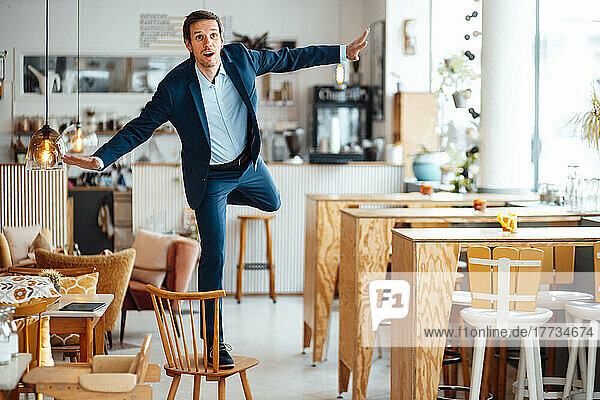 Businessman with arms outstretched standing on chair at cafe