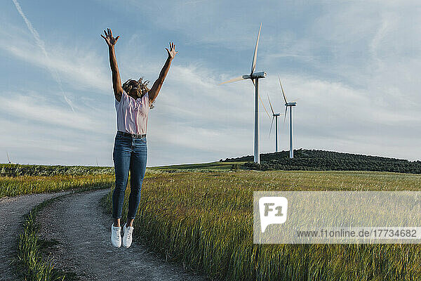 Young woman with arms raised jumping on footpath by meadow