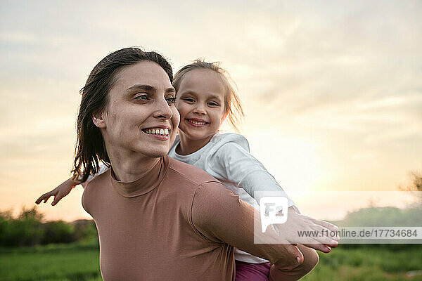 Smiling woman carrying girl piggyback in field