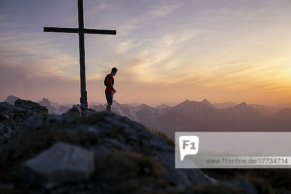 Hiker standing by summit cross on mountain