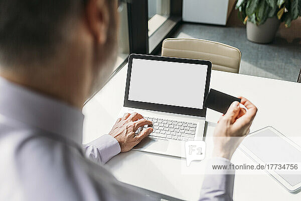 Businessman holding credit card making payment through laptop in office