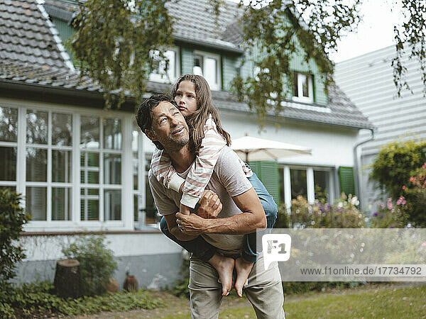 Father giving piggyback ride to daughter in front of house