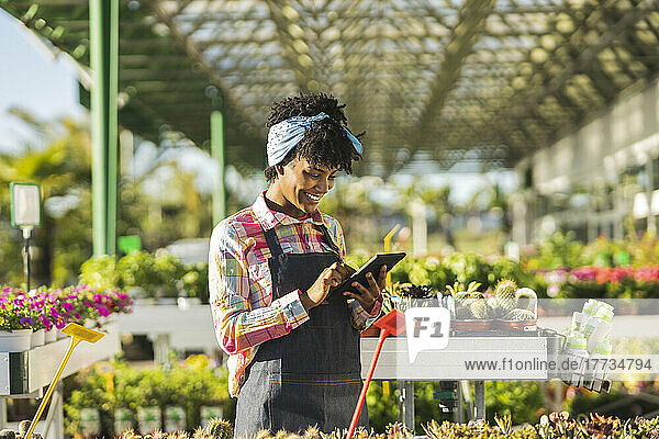Smiling gardener with bandana using tablet PC by plants at nursery
