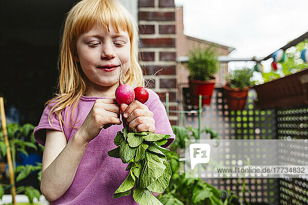 Girl with red hair looking at fresh radish on balcony