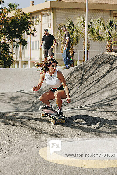 Young woman skateboarding at sports ramp with friends in background