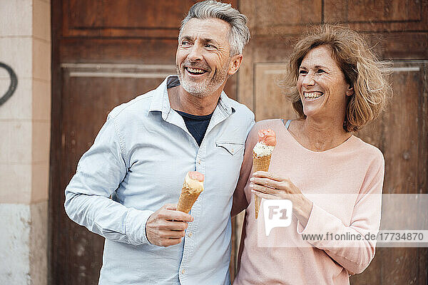 Cheerful mature couple with ice cream in front of door