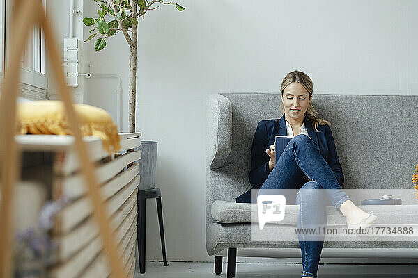 Lächelnde Geschäftsfrau mit Tablet-PC sitzt auf dem Sofa im Büro