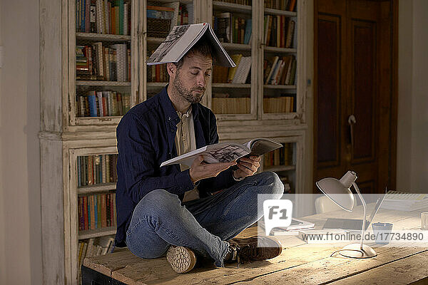 Man with book on head reading at home office