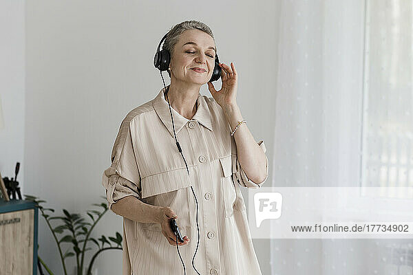 Mature woman wearing headphones listening to music at home